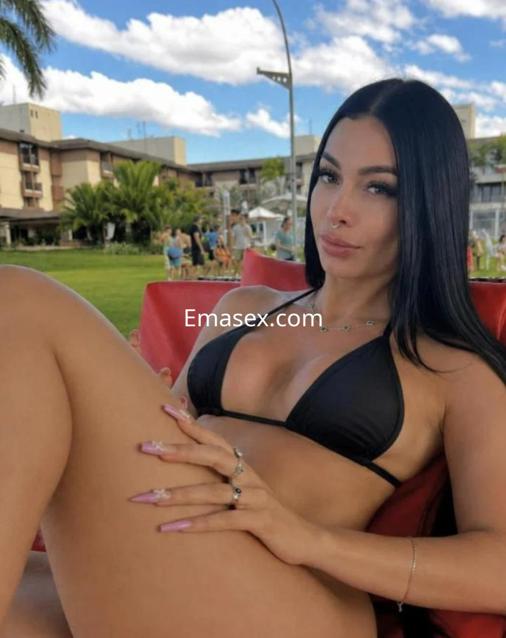 Puta en Las Palmas luce un bikini negro mientras se relaja en una silla, con el cabello largo y lacio.