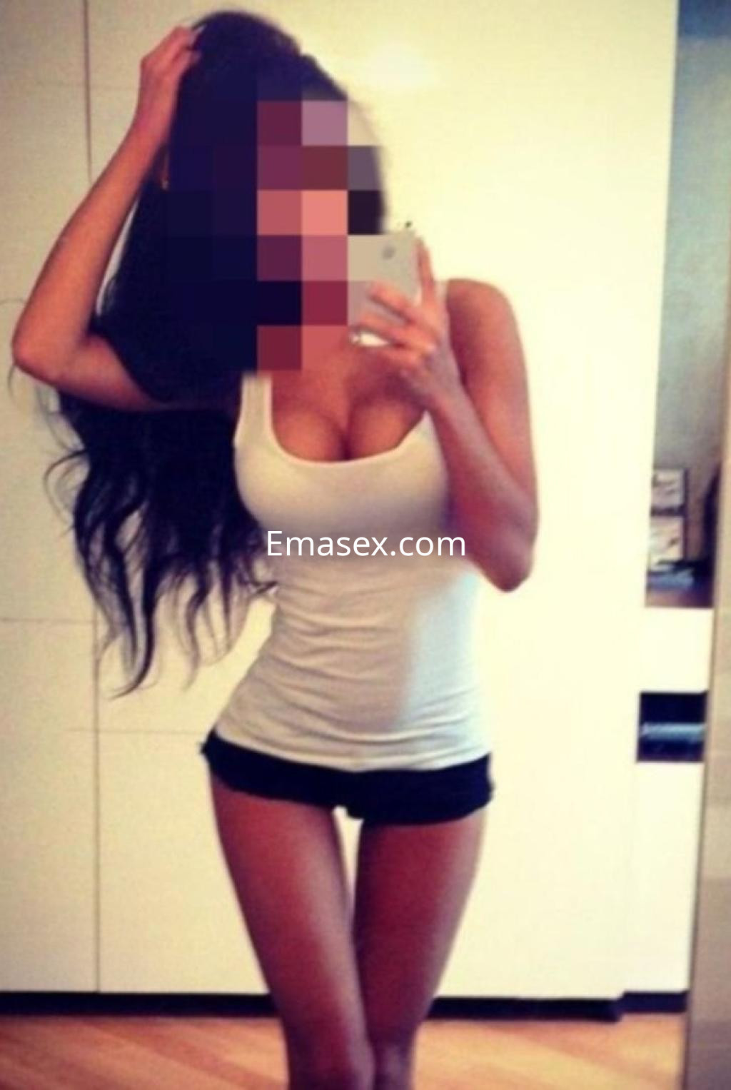 Puta en Huelva posa frente al espejo con camiseta blanca ajustada y shorts negros, mostrando su figura esbelta.