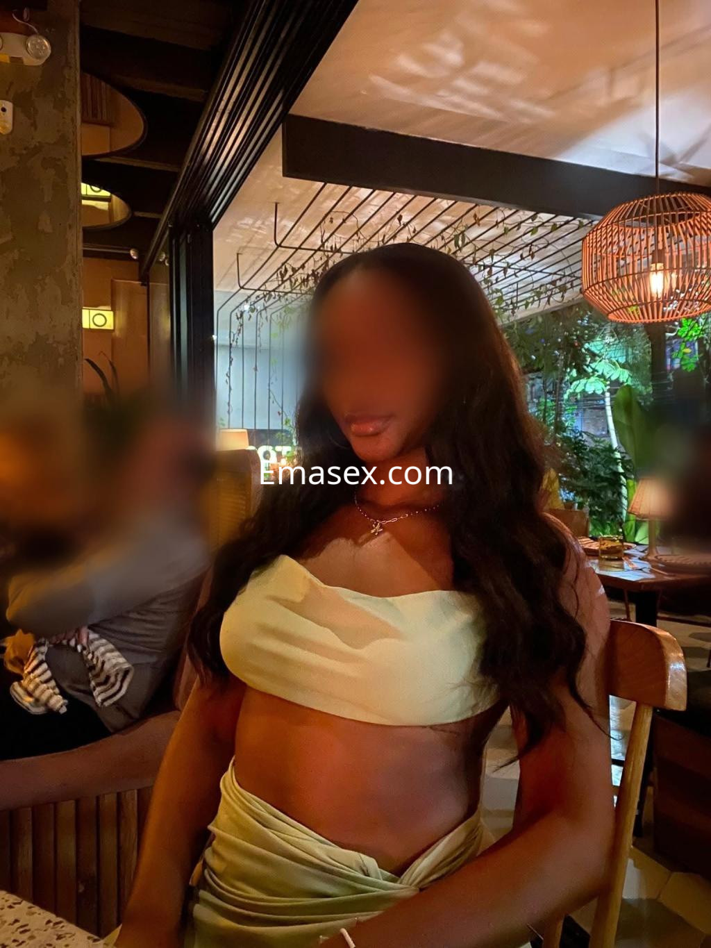 Escort en Pamplona con cabello largo y ondulado, vistiendo un top verde claro en un ambiente acogedor de restaurante.