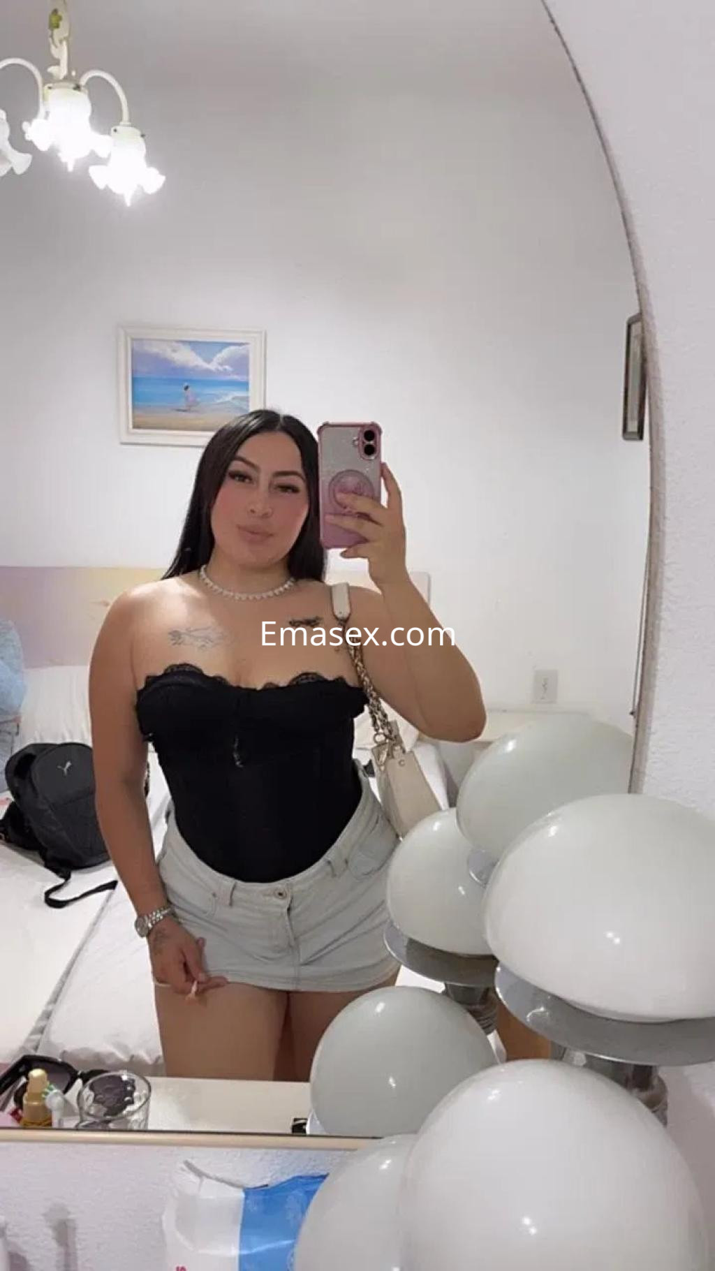 La puta está posando frente al espejo con un top negro y shorts claros en un entorno de habitación en Alicante.