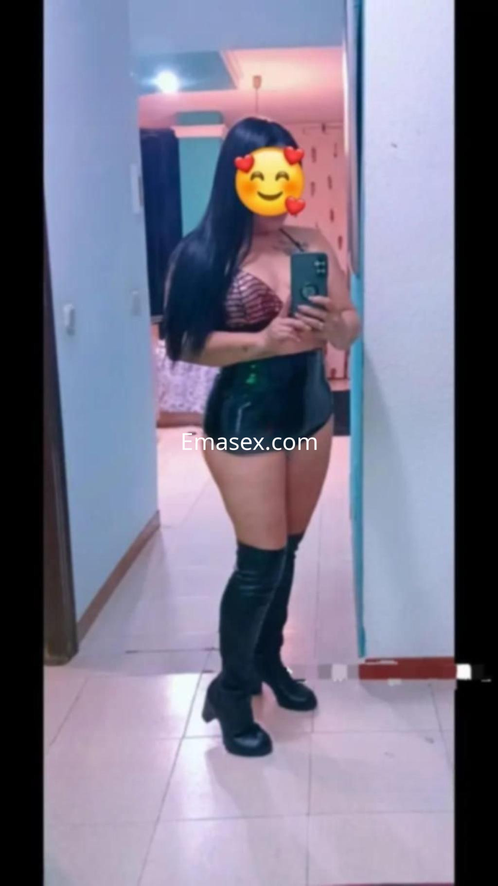 La puta se muestra en un espejo, vestida con un top de encaje y botas altas, en un entorno interior de Almería.