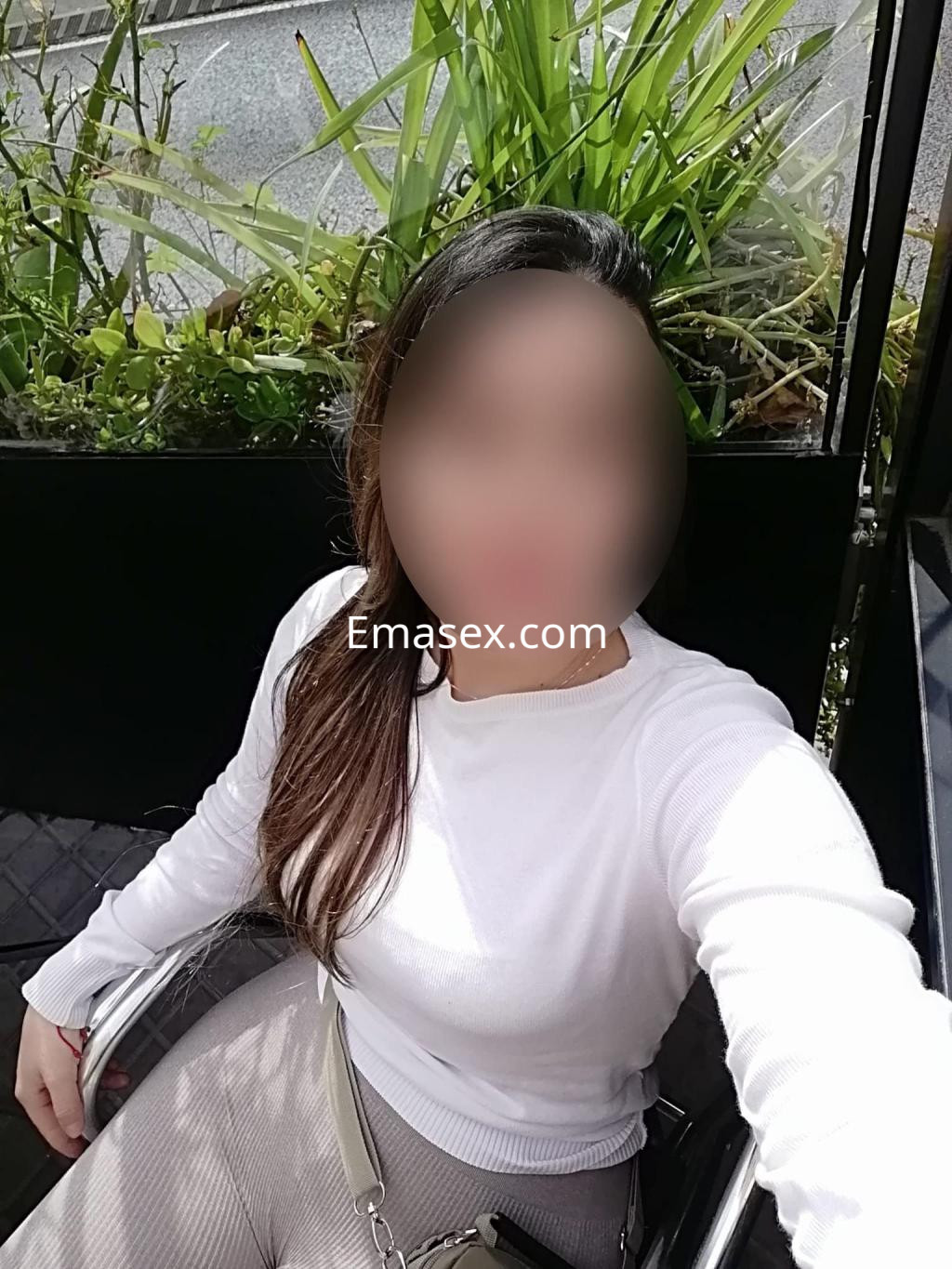 Escort en Barcelona, con cabello largo y oscuro, viste un suéter blanco y se encuentra sentada al aire libre.