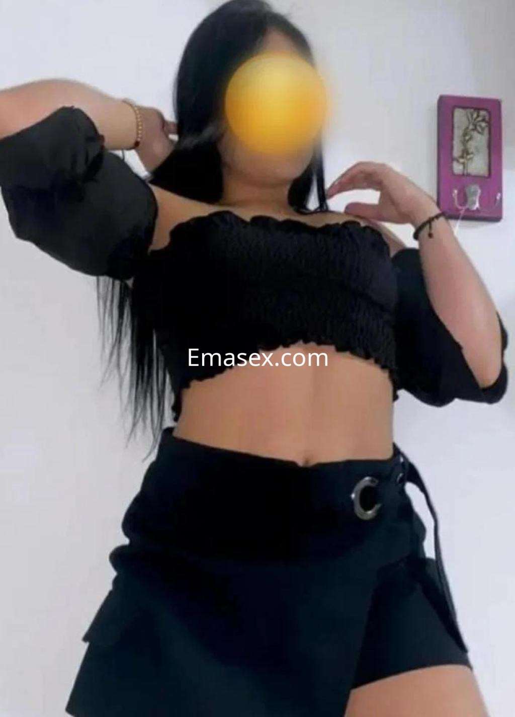 La puta en Coruña luce un top negro de mangas amplias y una falda corta, mostrando una pose coqueta.