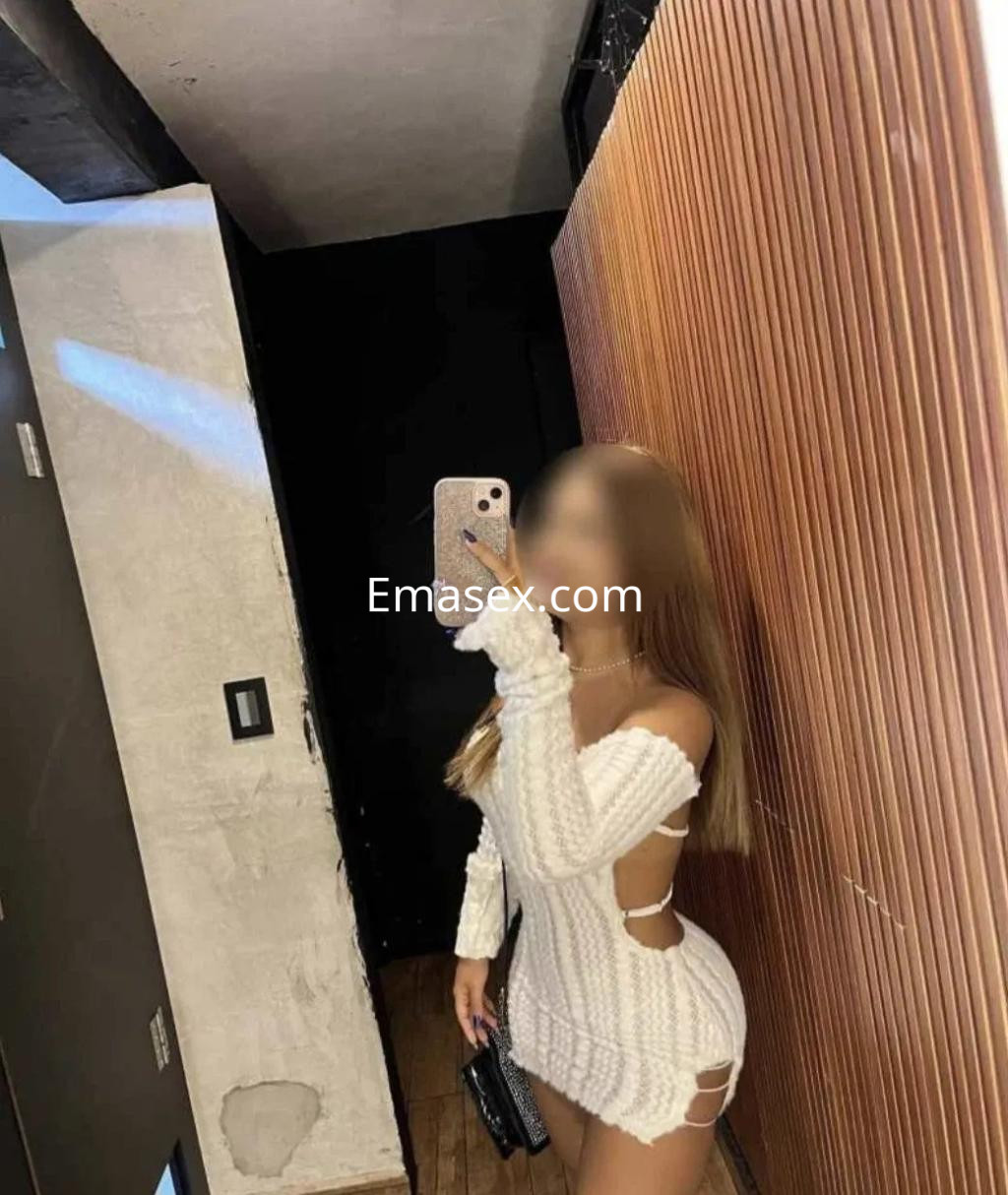 Puta en Coruña con un vestido blanco de punto, mostrando detalles de su piel y posando frente al espejo.