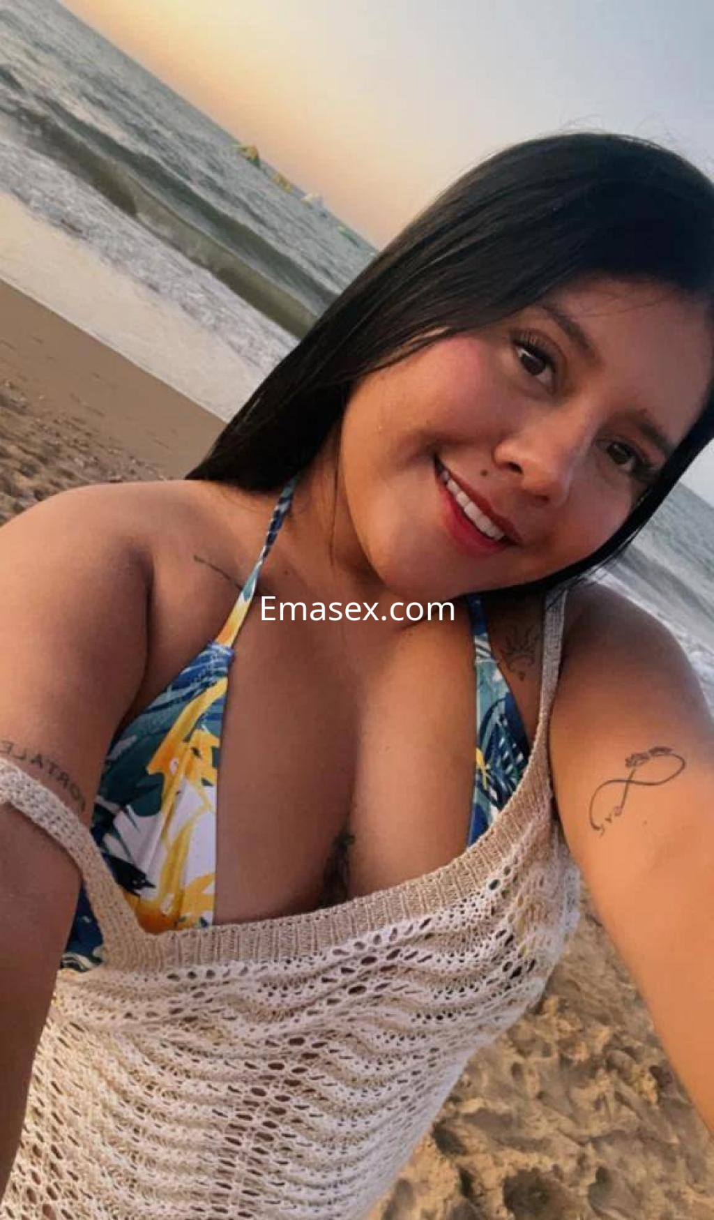 La puta se encuentra en la playa de Huelva, luciendo un bikini colorido y un suéter de crochet mientras sonríe.