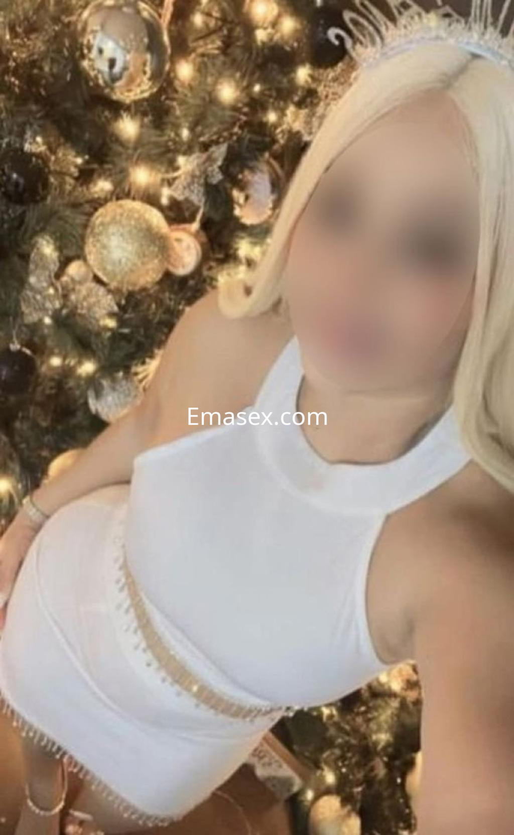 Escort en Oviedo vistiendo un vestido blanco ajustado, posando frente a un árbol de Navidad decorado.