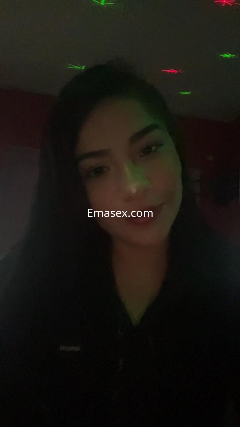 Escort en Oviedo con cabello oscuro y lacio, posando en un ambiente iluminado con luces de colores.