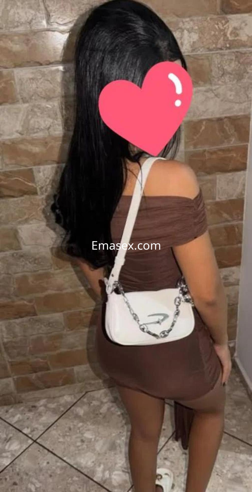 La puta lleva un vestido marrón ajustado y una bolsa blanca, posando de espaldas en un entorno doméstico en Sevilla.