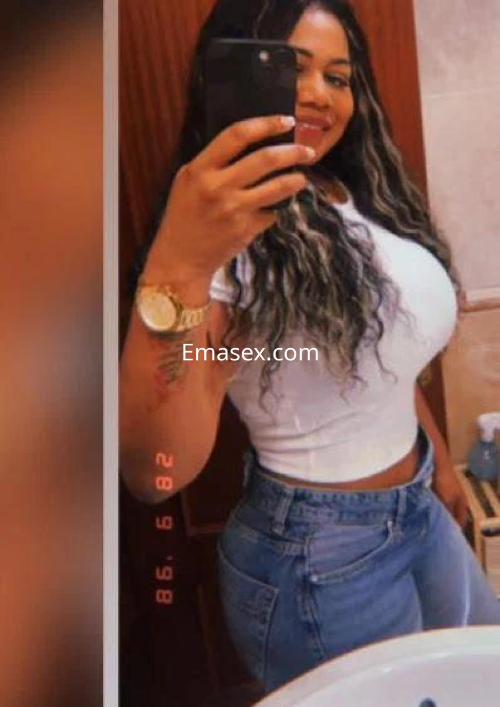 Puta con cabello largo y rizado, viste una camiseta blanca y jeans ajustados en un baño de Sevilla.