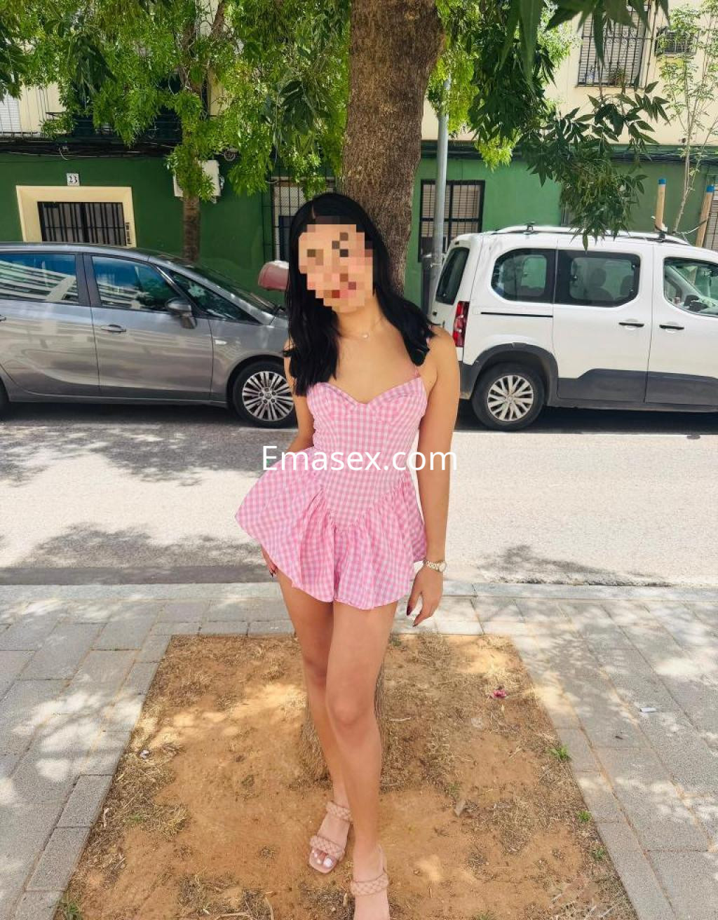 Escort en Sevilla, luciendo un vestido de cuadros rosas, de tirantes y con una falda amplia, en un entorno urbano.