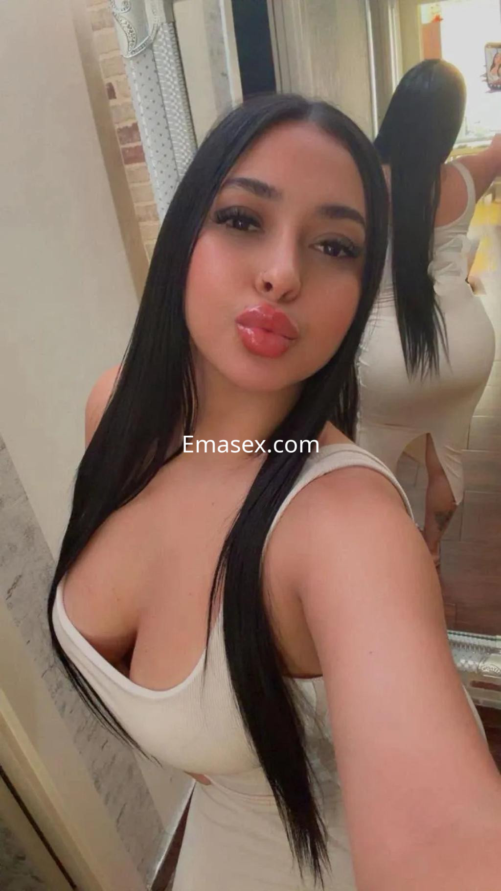 Puta posando en Valencia, viste un vestido blanco ajustado, con cabello largo y lacio, mostrando una expresión coqueta.