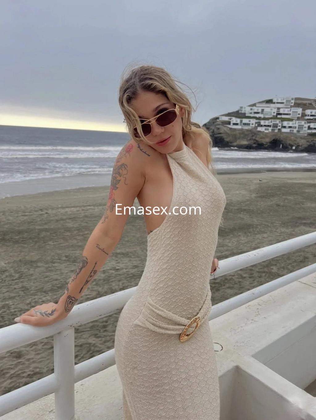 Puta posando en la playa de Valencia con un vestido claro y gafas de sol, mostrando sus tatuajes.