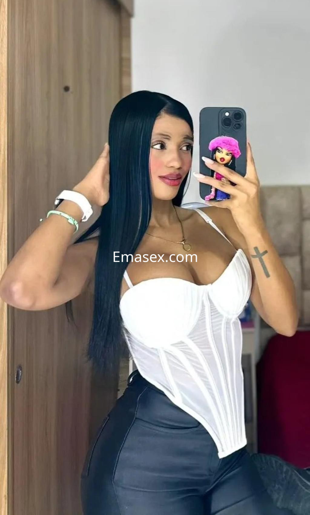 La puta en Málaga luce un corset blanco ajustado y pantalones negros, mostrando una pose coqueta frente al espejo.