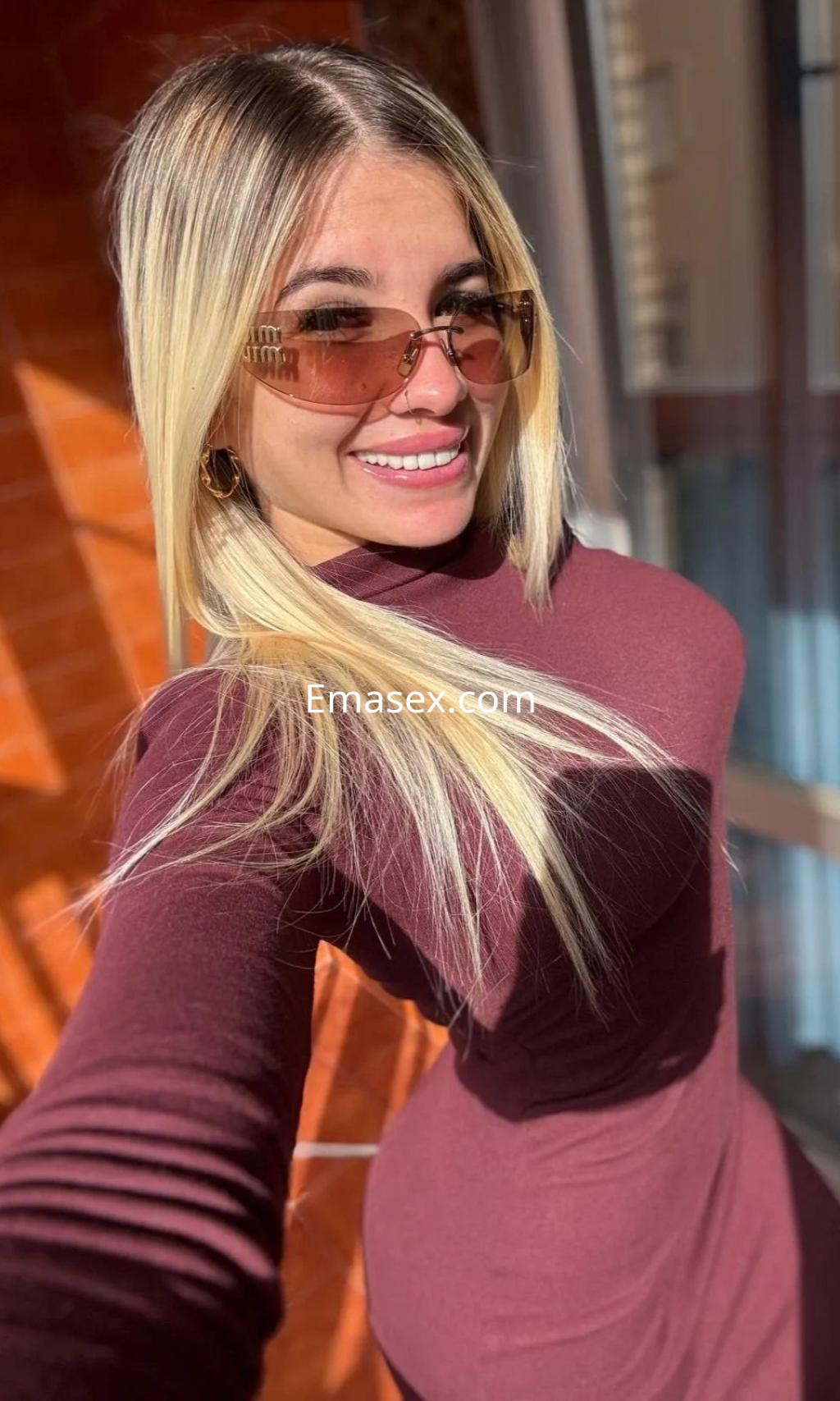 La puta sonríe mientras posa con un vestido ajustado de color burdeos y gafas de sol en Málaga.