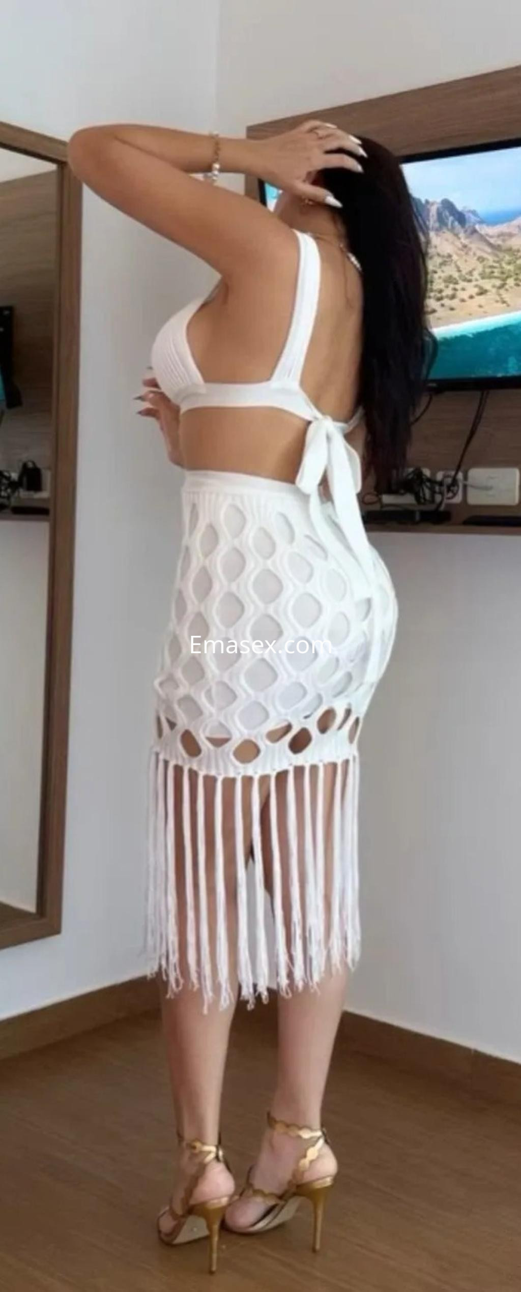 Puta de espaldas en Oviedo, luciendo un vestido blanco con flecos y tacones dorados en un entorno interior.