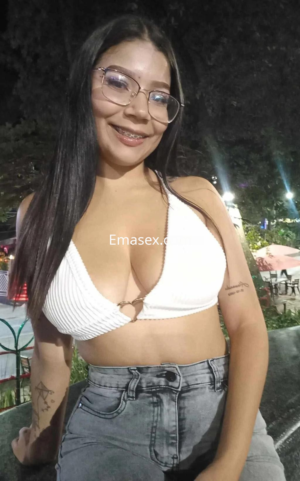 Escort en Oviedo con cabello largo y lacio, usando un top blanco y pantalones de mezclilla, sonriendo en un parque.