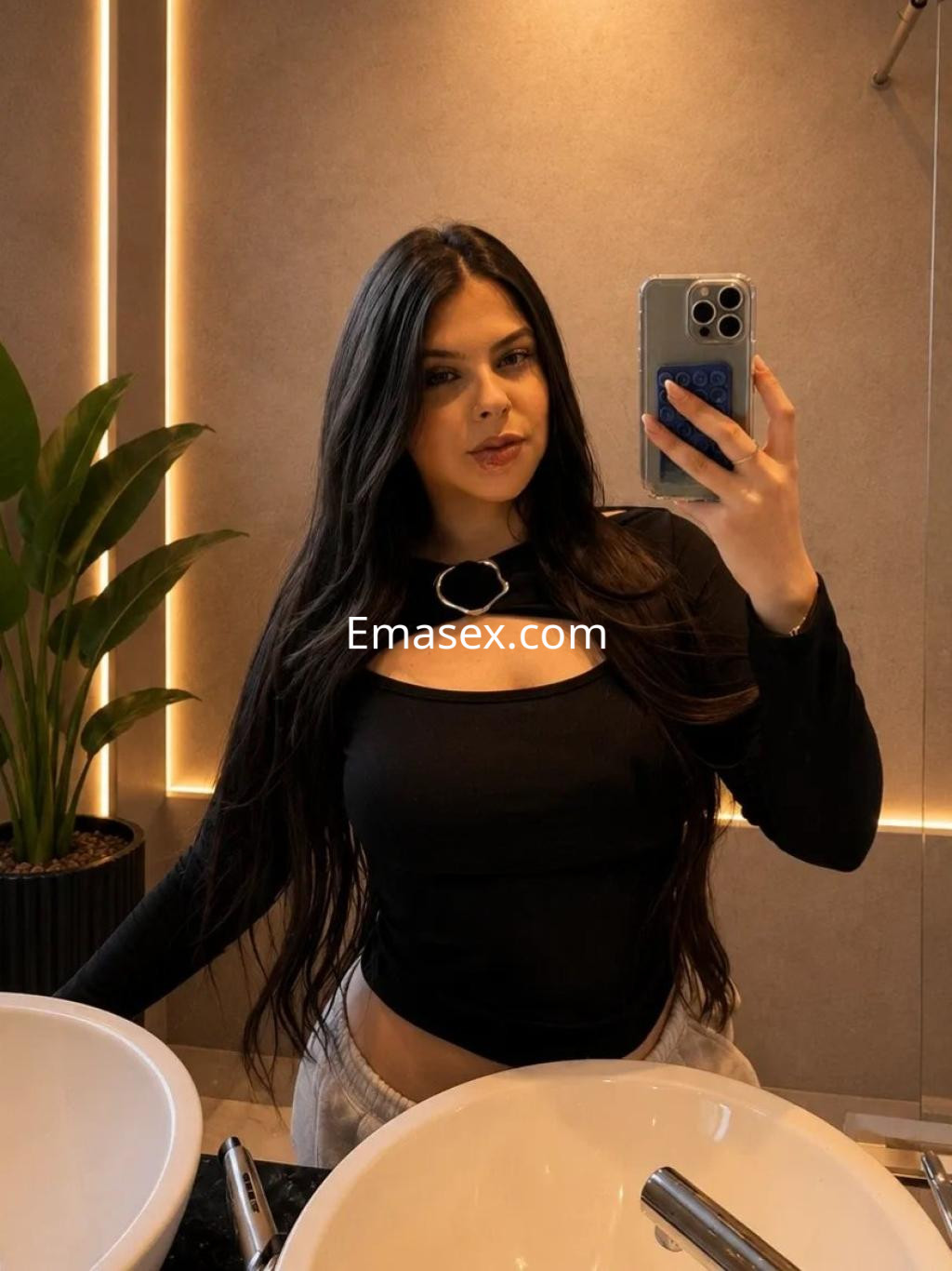 Escort en Coruña, con cabello largo y oscuro, viste una blusa negra con un corte en el pecho y se toma un autorretrato.
