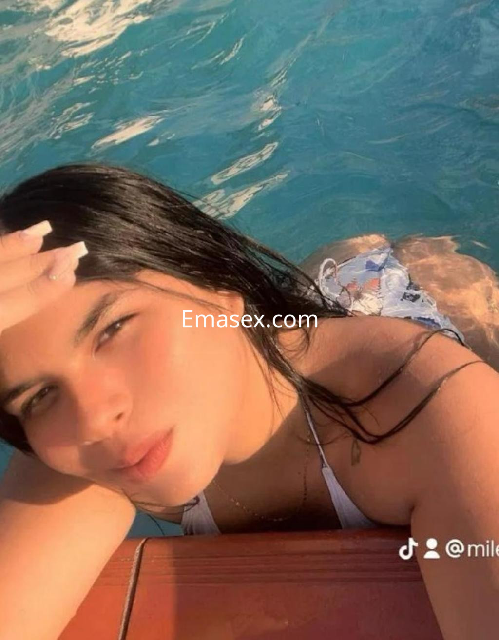 Puta posando en la piscina de Barcelona, con cabello oscuro y un bañador blanco, luciendo relajada y sonriente.