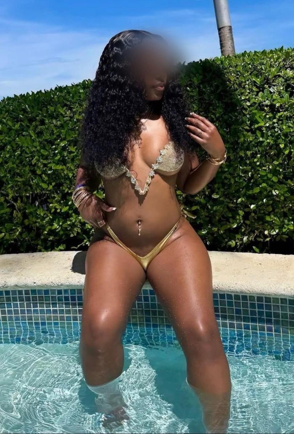 Puta posando en la piscina con un bikini dorado, rodeada de vegetación, mostrando su figura tonificada en Pamplona.