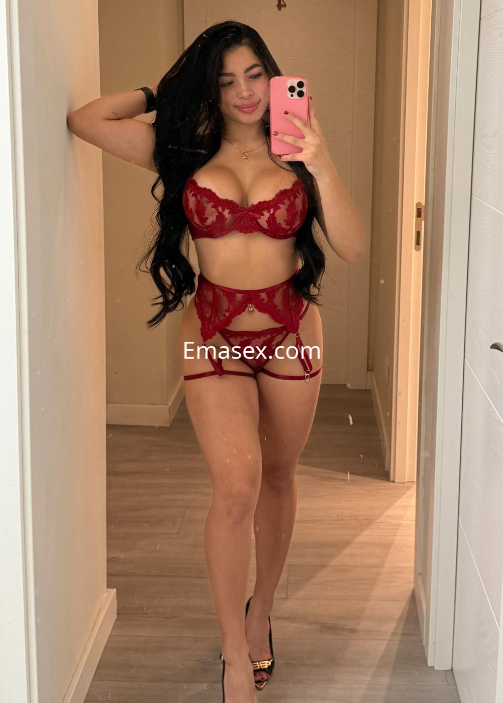 Escort en Zaragoza con cabello largo y lacio, luce un conjunto de lencería roja mientras se toma una selfie en un espejo.