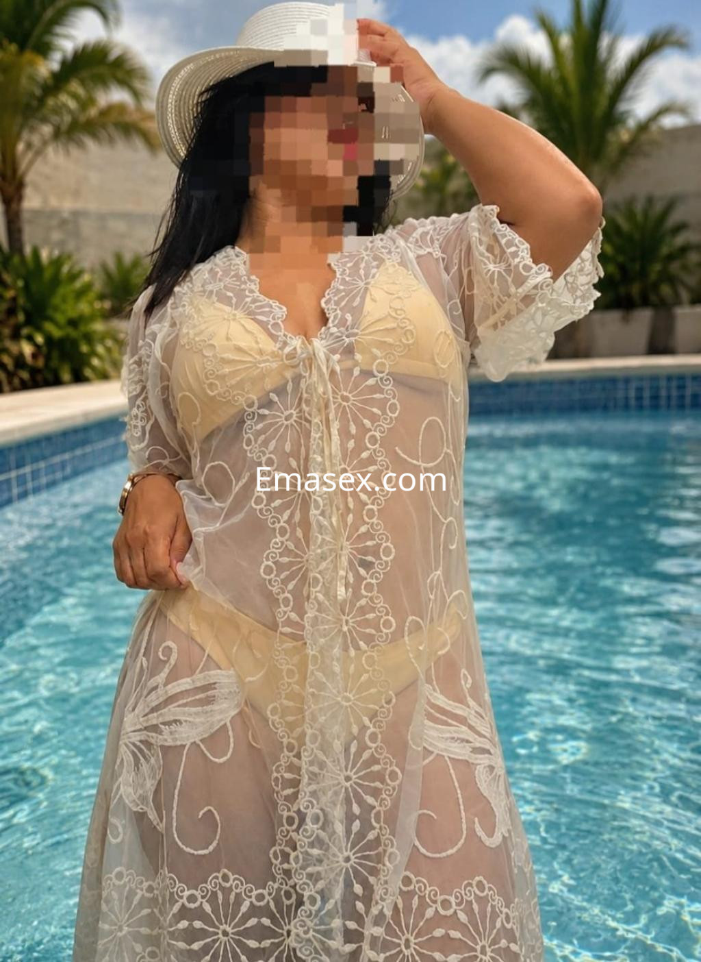 Escort en Pamplona luciendo un vestido blanco transparente con detalles de encaje, posando junto a una piscina.