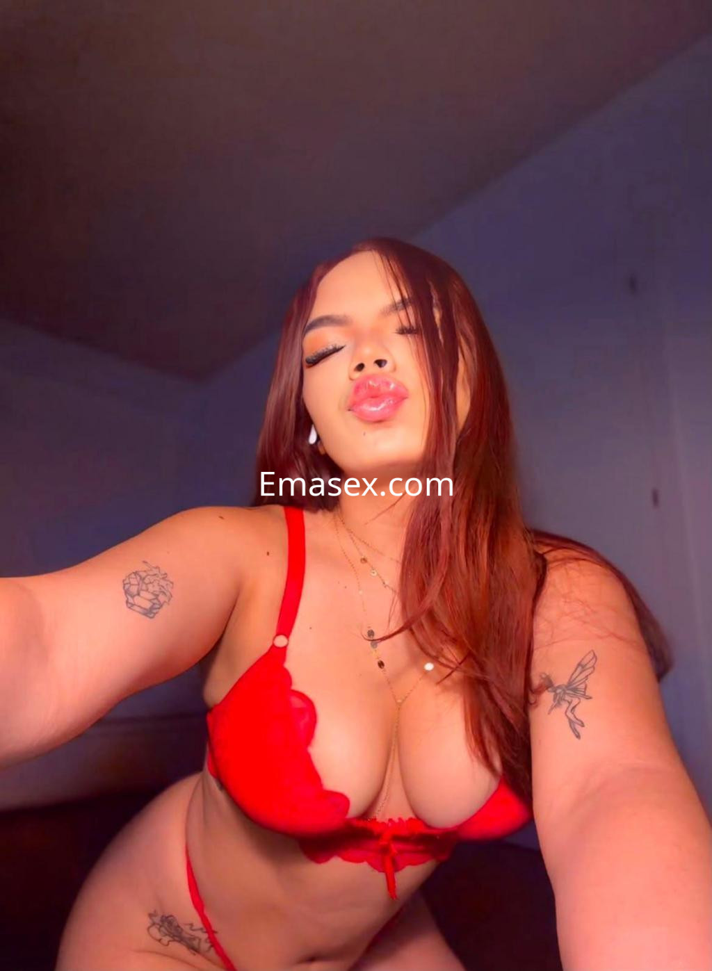 Escort en Almería posando con lencería roja, cabello largo y lacio, con un fondo suave y luz tenue.