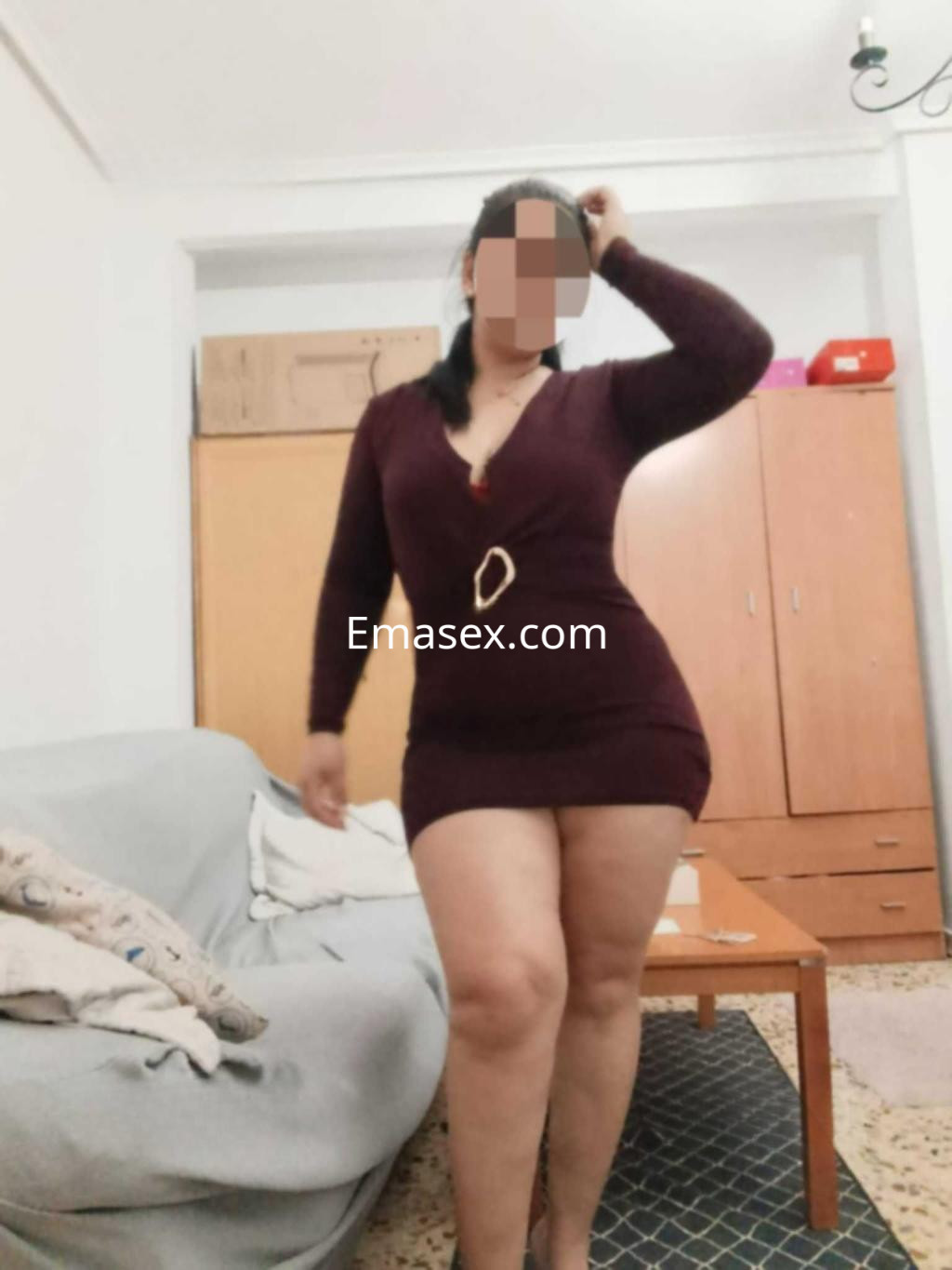 Escort en Albacete posando en un salón, viste un vestido ajustado de color burdeos y tacones altos.