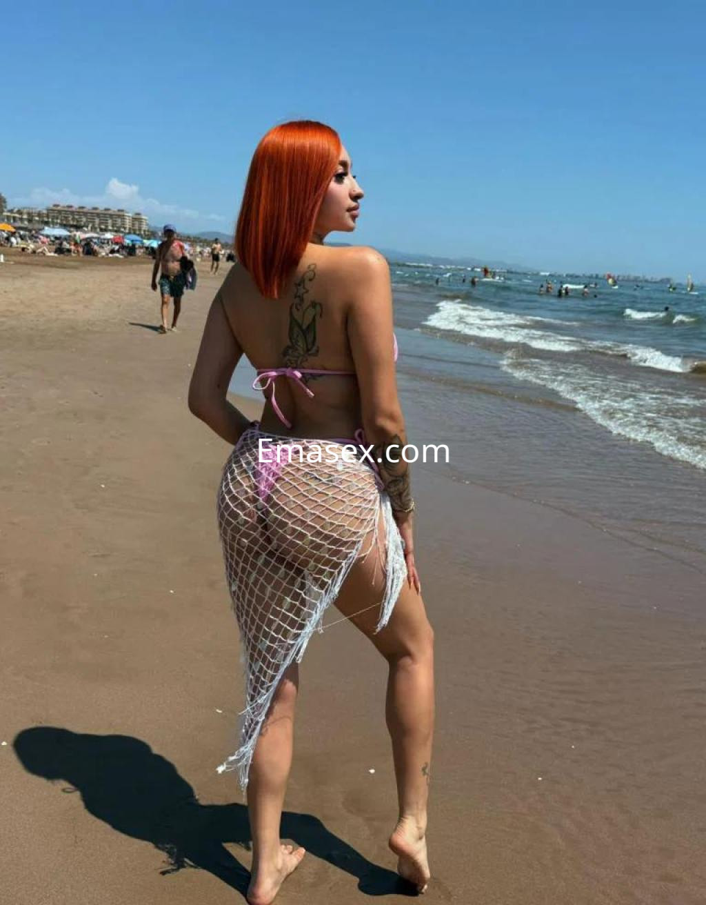 Puta de cabello rojo, con un bikini y una falda de red, posando de espaldas en la playa de Almería.
