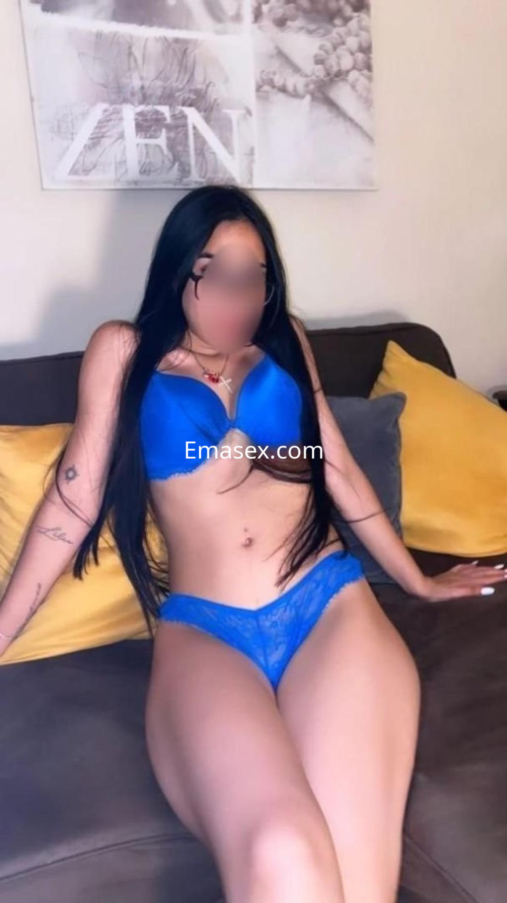 Escort en Almería luciendo un conjunto de lencería azul, sentada en un sofá con almohadas decorativas.