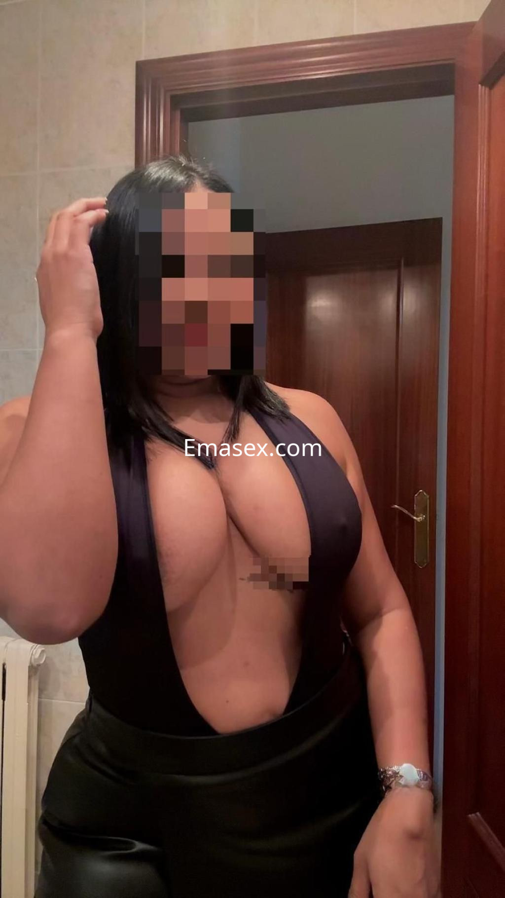 Escort en Badajoz con cabello oscuro, viste un body ajustado y pantalones de cuero, posando en un baño.