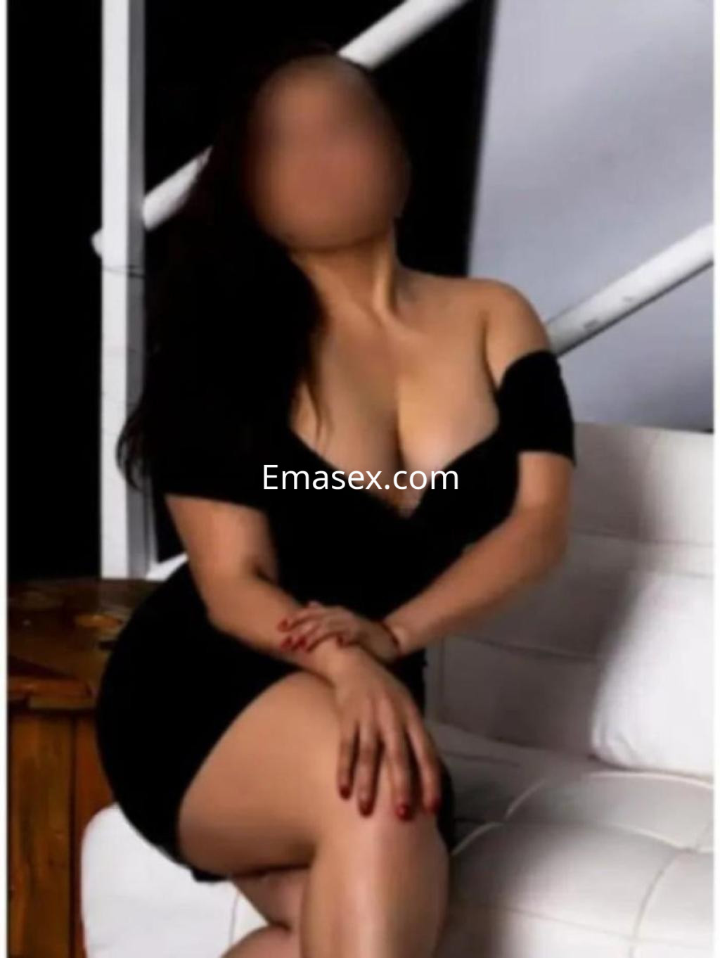 La escort se encuentra sentada en un sofá en Córdoba, luciendo un vestido negro ajustado que destaca sus curvas.
