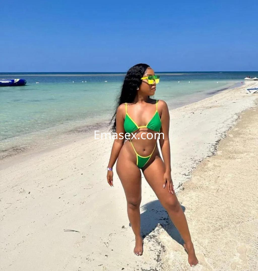 Puta en Córdoba luciendo un bikini verde en la playa, con gafas de sol y el mar de fondo.