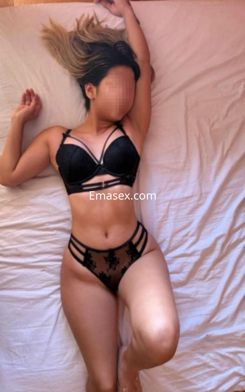 Puta en Córdoba, posando sobre una cama con lencería negra que resalta su figura y cabello largo.