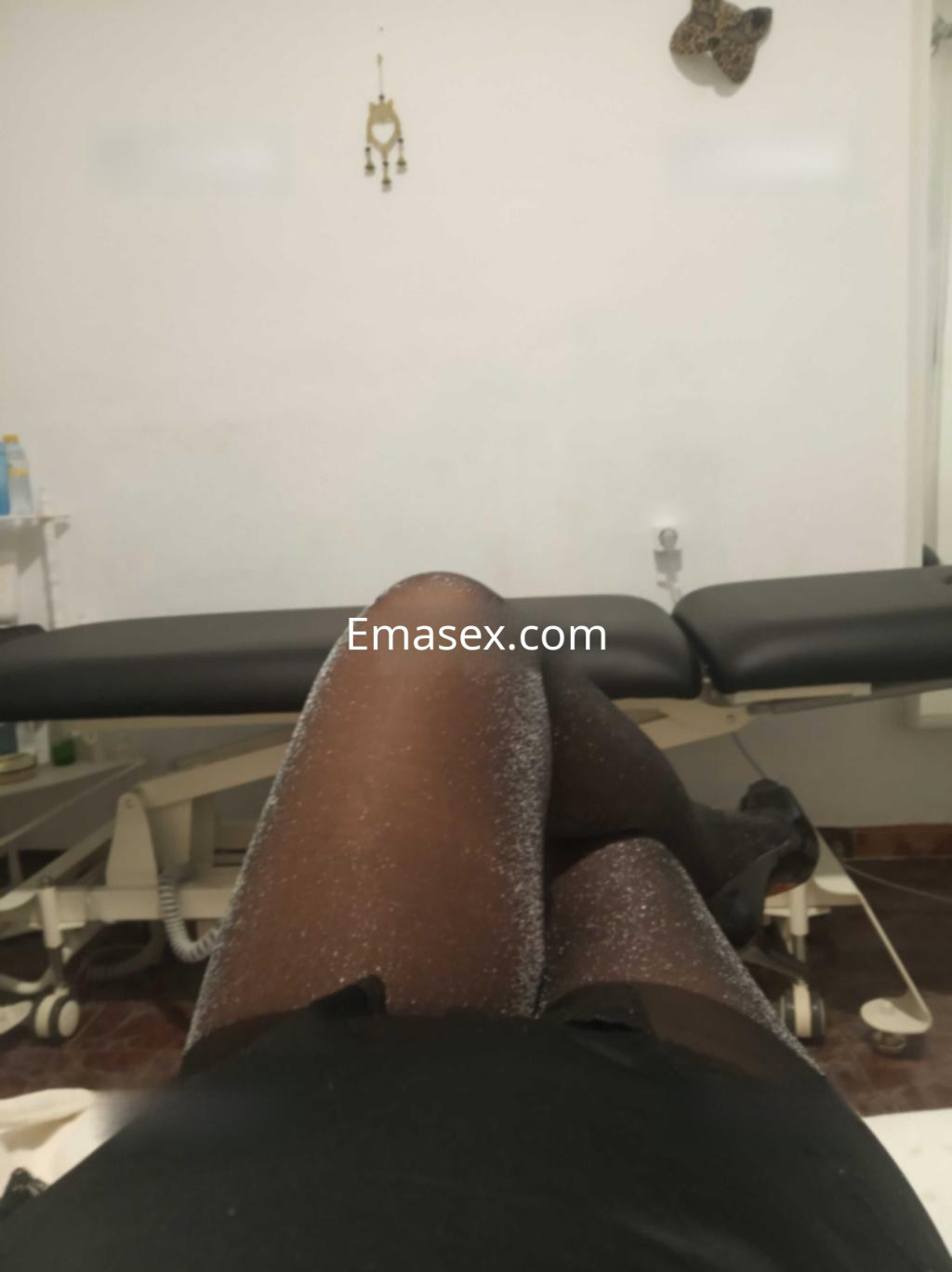 La puta en Granada luce medias brillantes y un vestido negro, reclinada en un entorno de masaje.