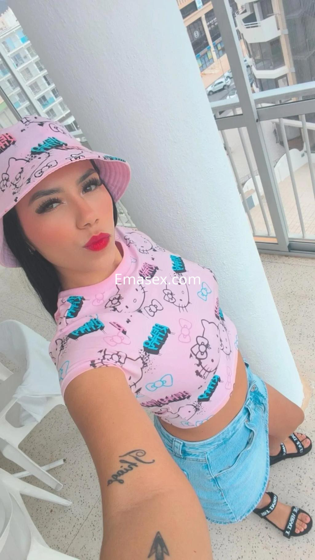 Escort en Murcia, luciendo una camiseta rosa con estampado divertido, falda de mezclilla y gorra a juego.