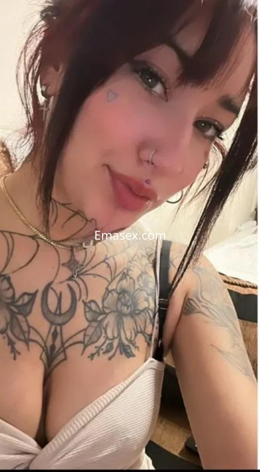 Escort en Vigo con cabello corto y rojizo, luciendo un top claro y mostrando tatuajes en el pecho y cuello.