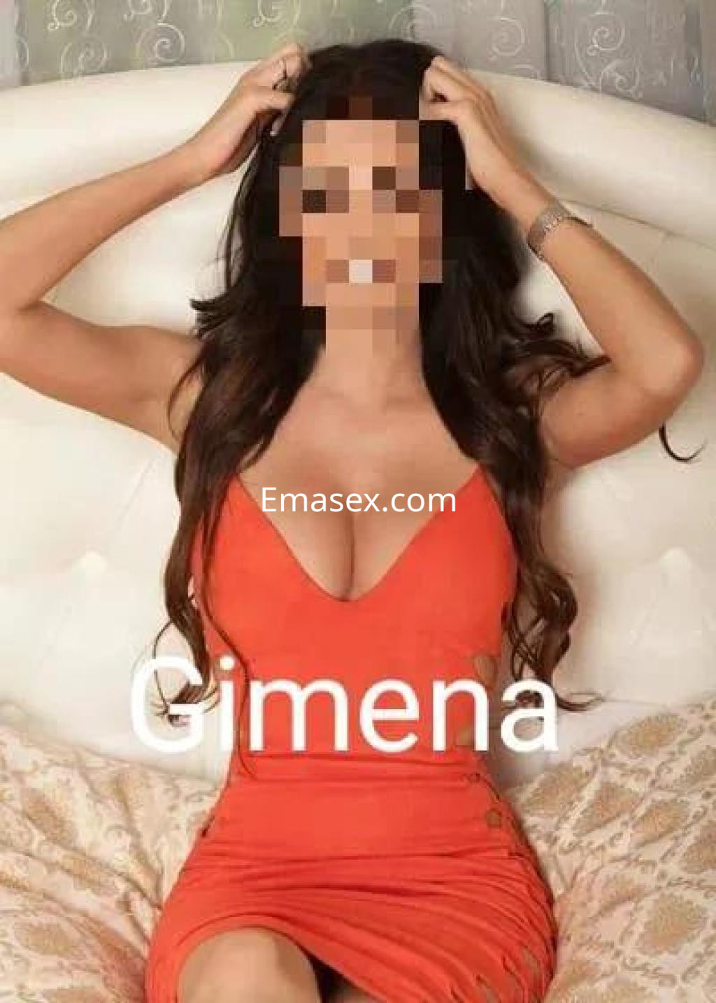 Escort en Sevilla con vestido ajustado de color naranja, posando en un sofá con una expresión relajada.