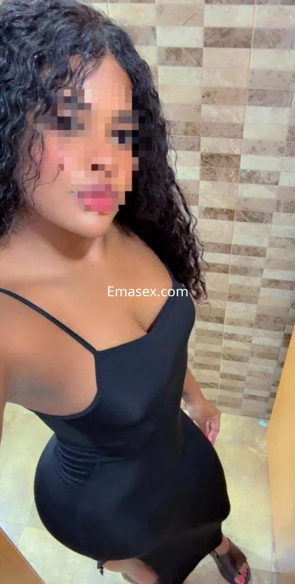 Puta posando en un baño con un vestido negro ajustado, cabello rizado y un fondo de azulejos en Tarragona.