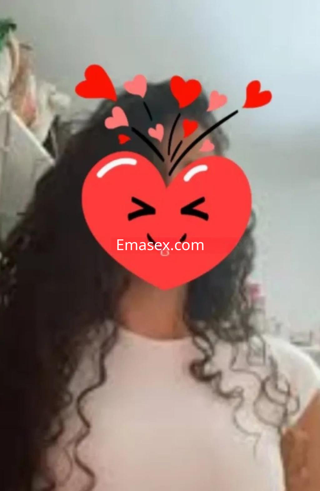 Puta con cabello rizado y oscuro, viste una camiseta blanca en un entorno interior de Málaga.
