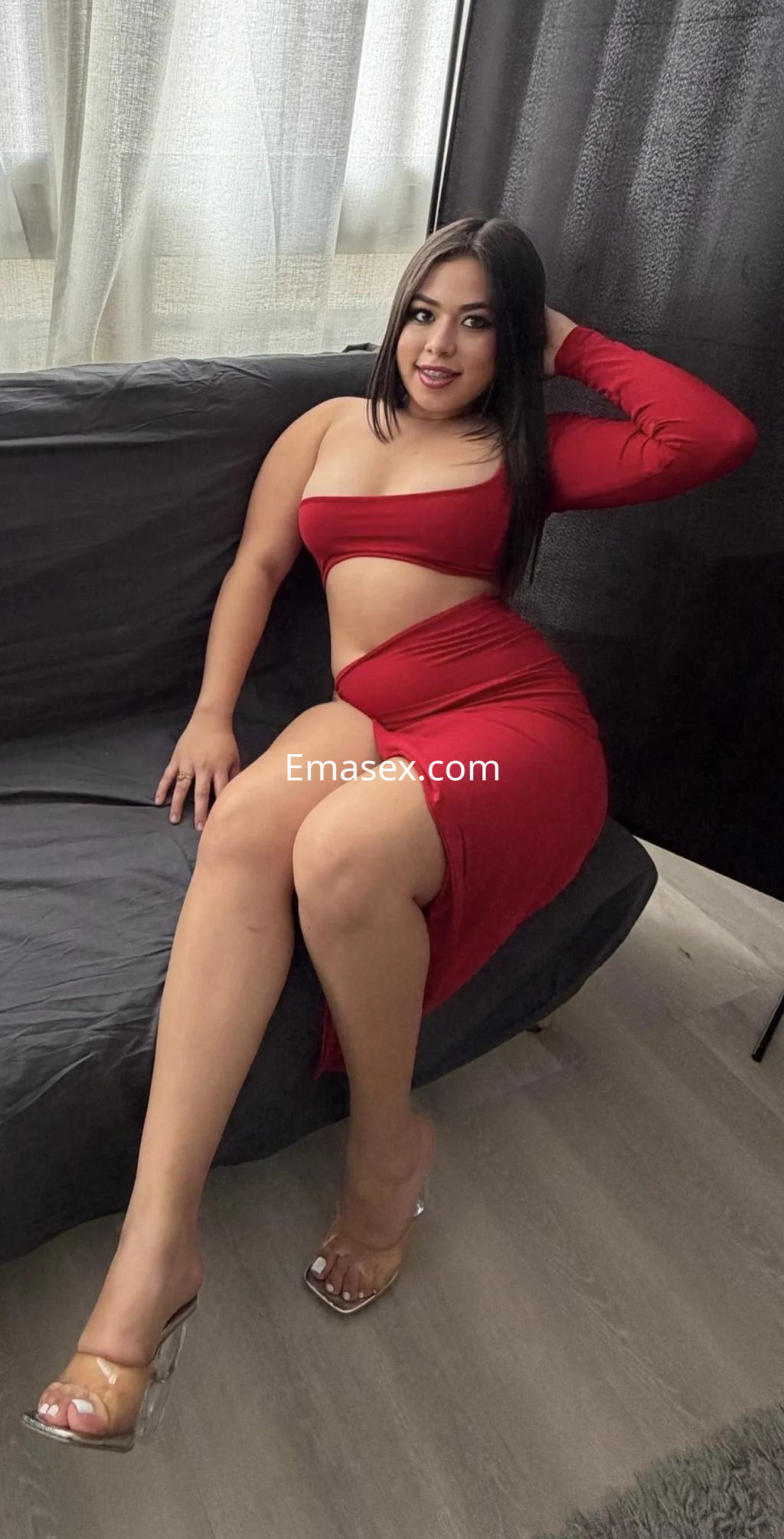 Puta sentada en un sofá, vistiendo un vestido rojo ajustado con una pierna al descubierto, en Málaga.