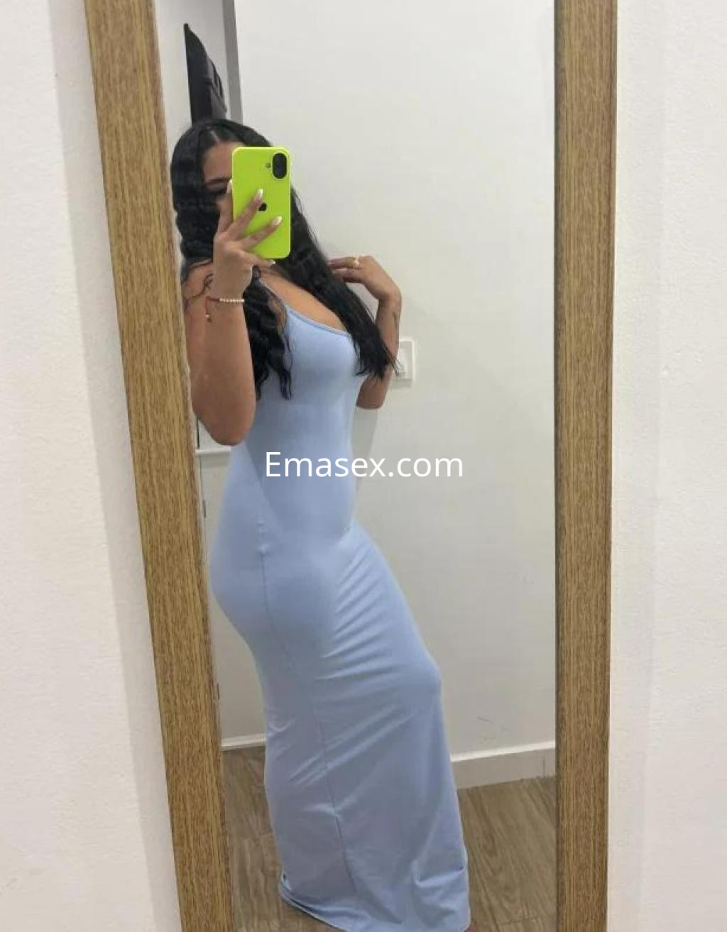La puta posa frente a un espejo, luciendo un vestido largo azul claro y mostrando su figura en Córdoba.