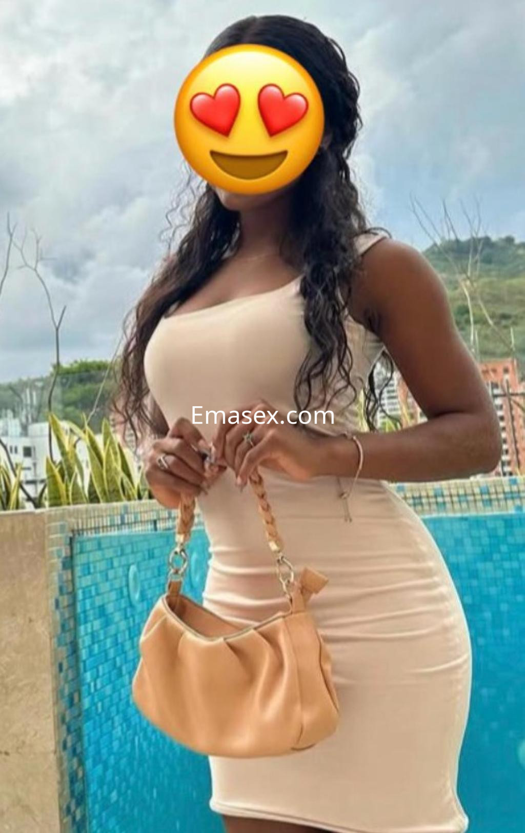 Escort en Santander viste un vestido ajustado color beige y sostiene un bolso, con un fondo de piscina y montañas.