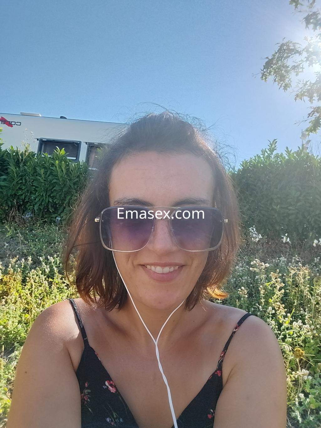 Puta sonriente con gafas grandes, llevando un vestido sin mangas, en un entorno natural de Coruña.