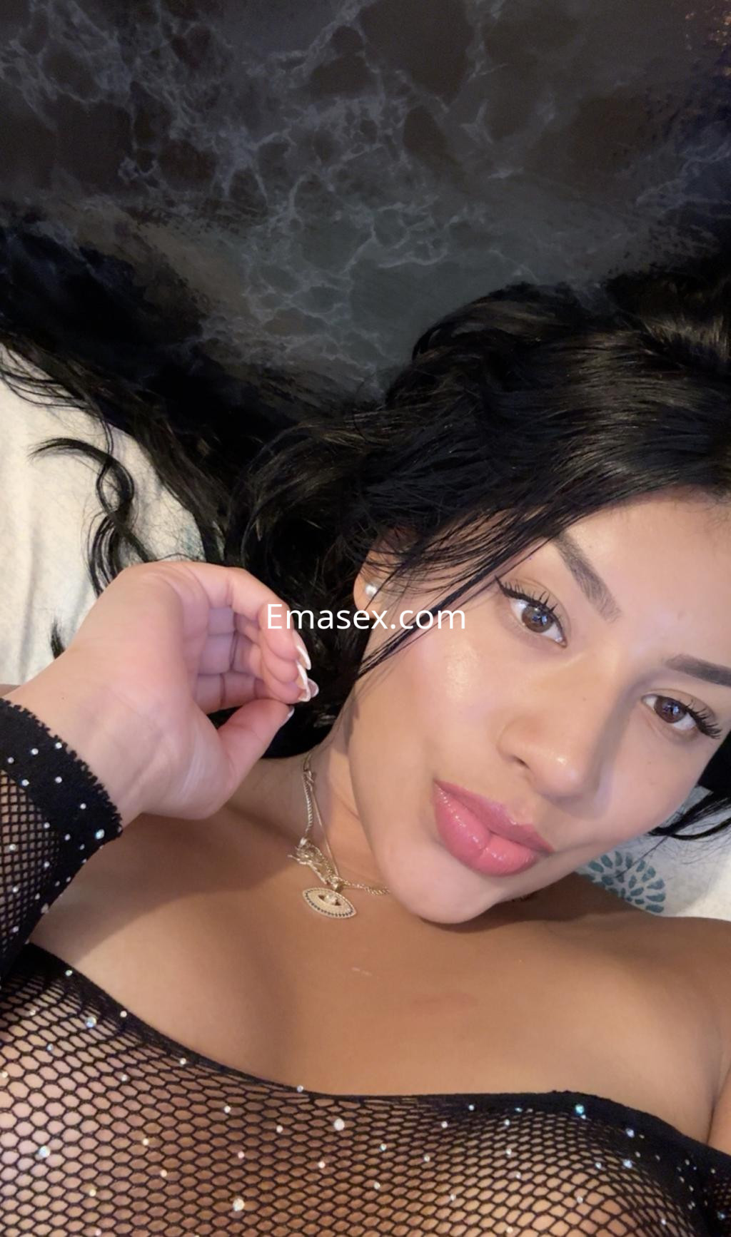 Escort en Oviedo recostada sobre una superficie suave, luciendo un top de malla negra y un maquillaje sutil.