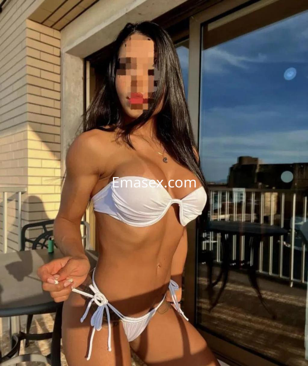 Puta en Alicante con bikini blanco, posando en un balcón con luz natural y pelo largo suelto.