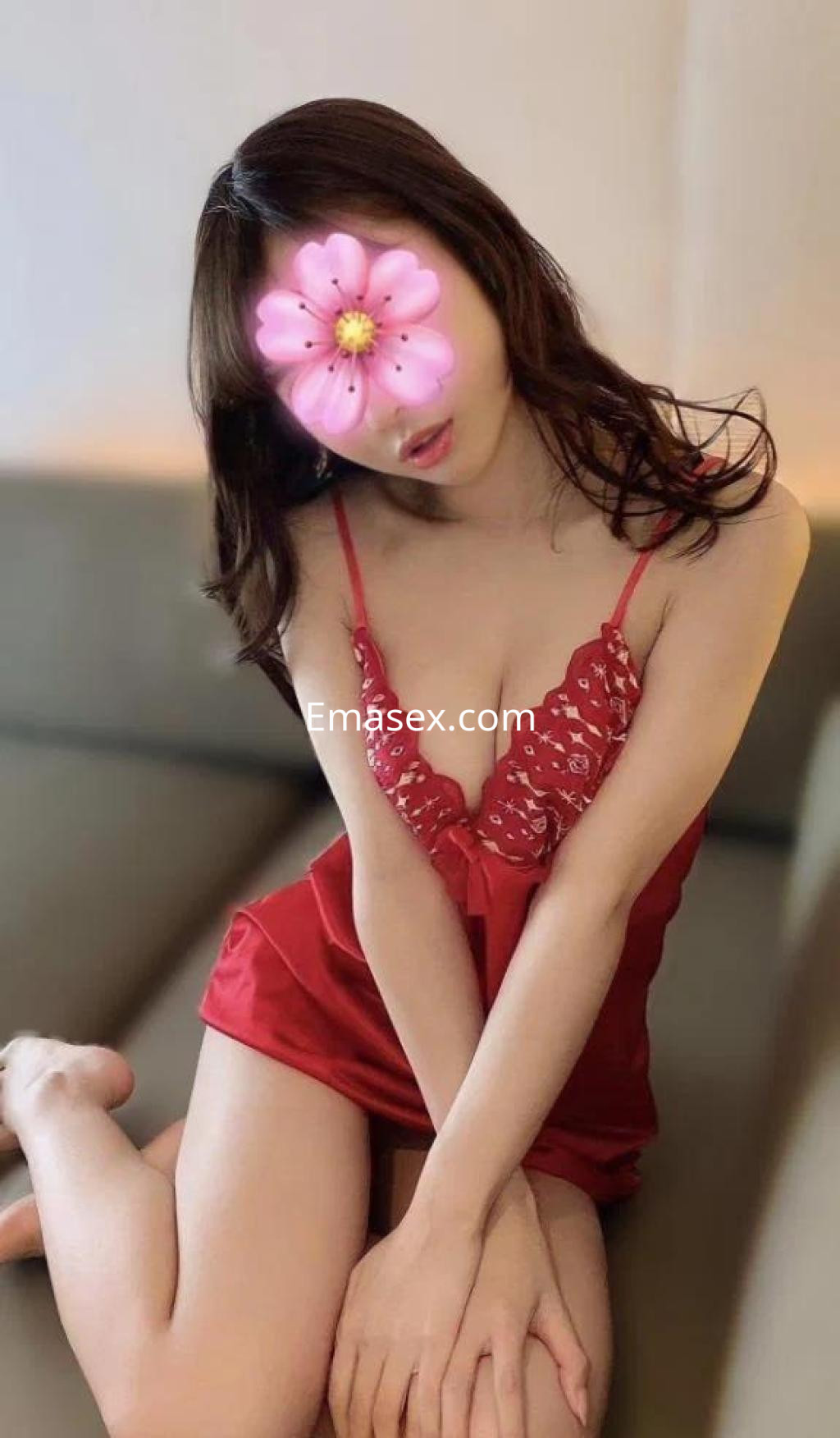 Puta en Barcelona, sentada en un sofá, vistiendo un camisón rojo con detalles y cabello lacio oscuro.