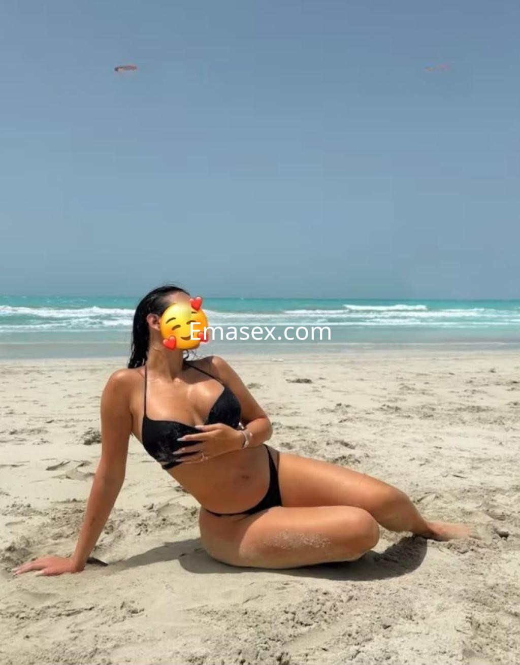 Puta en Córdoba sentada en la arena de la playa, luciendo un bikini negro y disfrutando del sol.