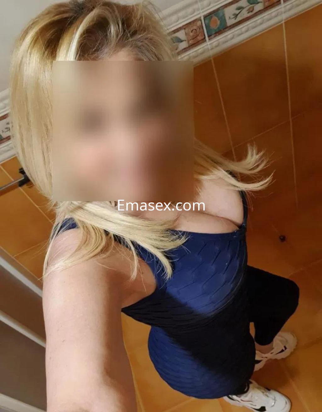 La puta se muestra de pie en un baño con un vestido azul que resalta su figura y zapatillas blancas, en Coruña.