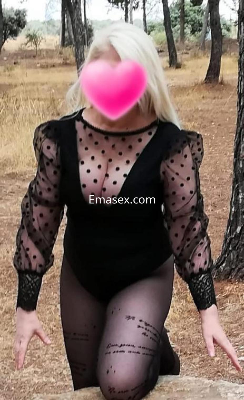 Escort en Granada, con cabello rubio y top negro de mangas abullonadas, posando en un entorno natural.