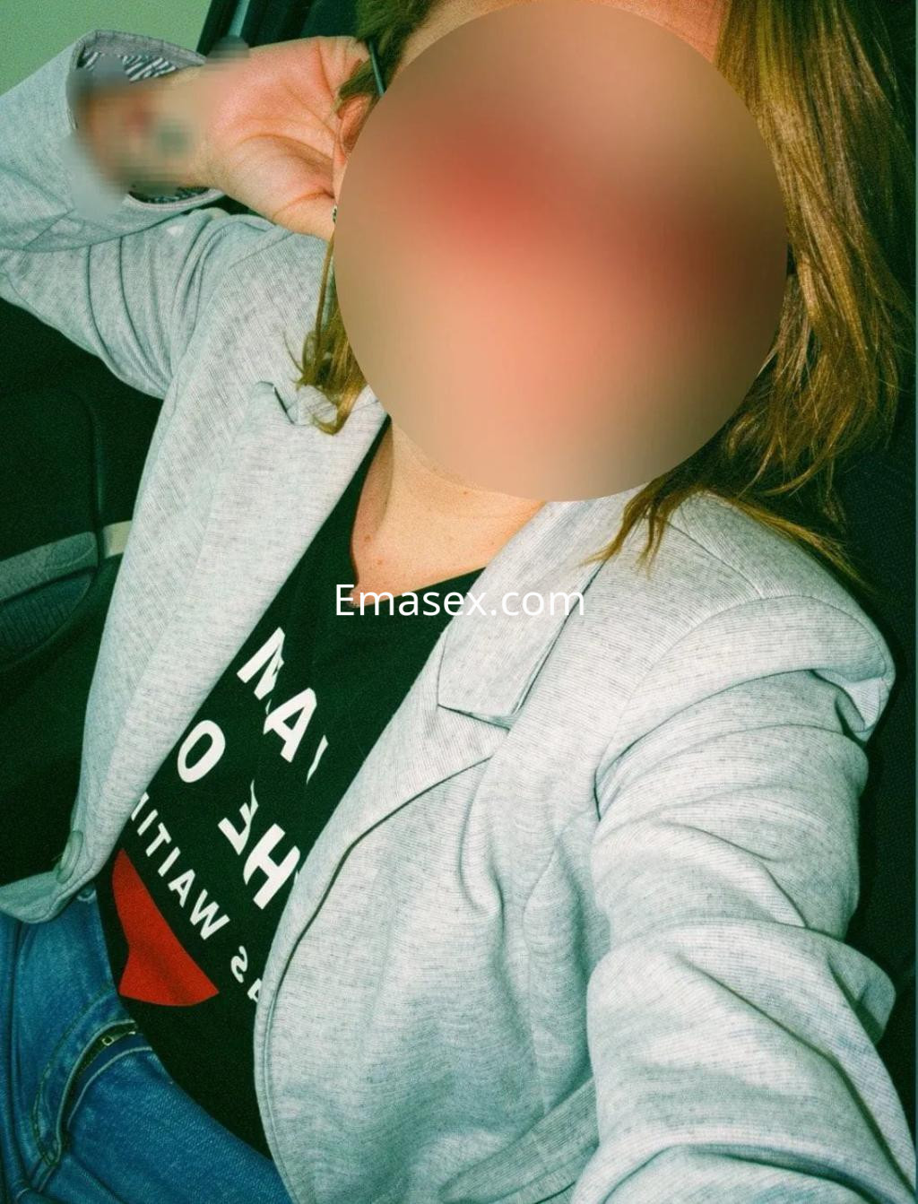 Escort en Madrid posa con una chaqueta gris y camiseta negra, sentada en un vehículo con una expresión relajada.